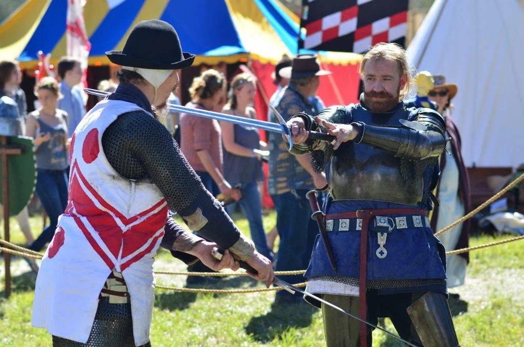 Two fighters, full concentration, blades crossed. The colourful tents behind them do nothing to diminish how real the steel looks.