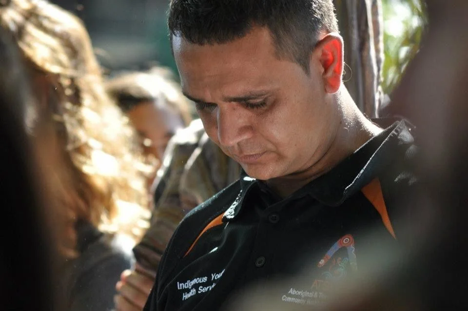 He stood with his head bowed while a speaker addressed the gathering. The uniform — Indigenous Youth Health Service — told one story. The posture told another.