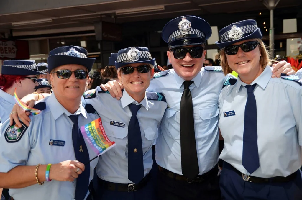 Four Queensland police officers in full uniform, arms around each other, holding rainbow flags and grinning. Context is everything.
