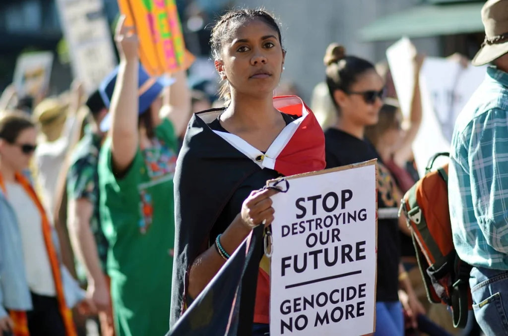 She marched with the Aboriginal flag over her shoulders and a sign reading 'Stop Destroying Our Future'. The composure on her face was the most powerful thing in the frame.