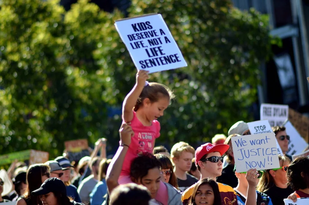 A small girl held up on someone's shoulders, holding a sign that says 'Kids Deserve a Life, Not a Life Sentence'. She could not yet read what it said.