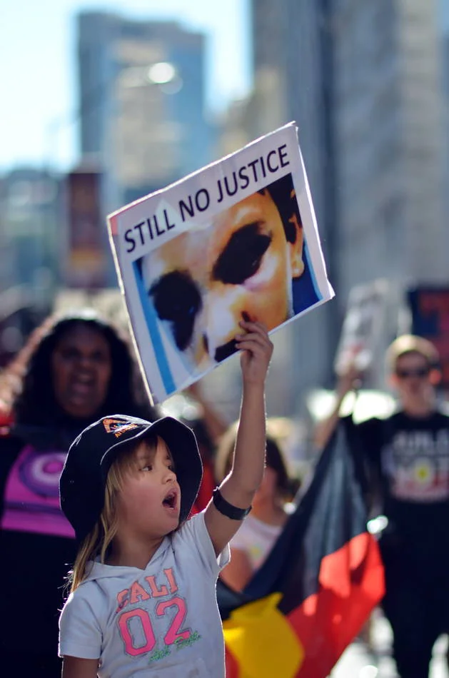 She held the sign above her head with both hands and shouted something I could not hear over the crowd. The photograph heard it instead.