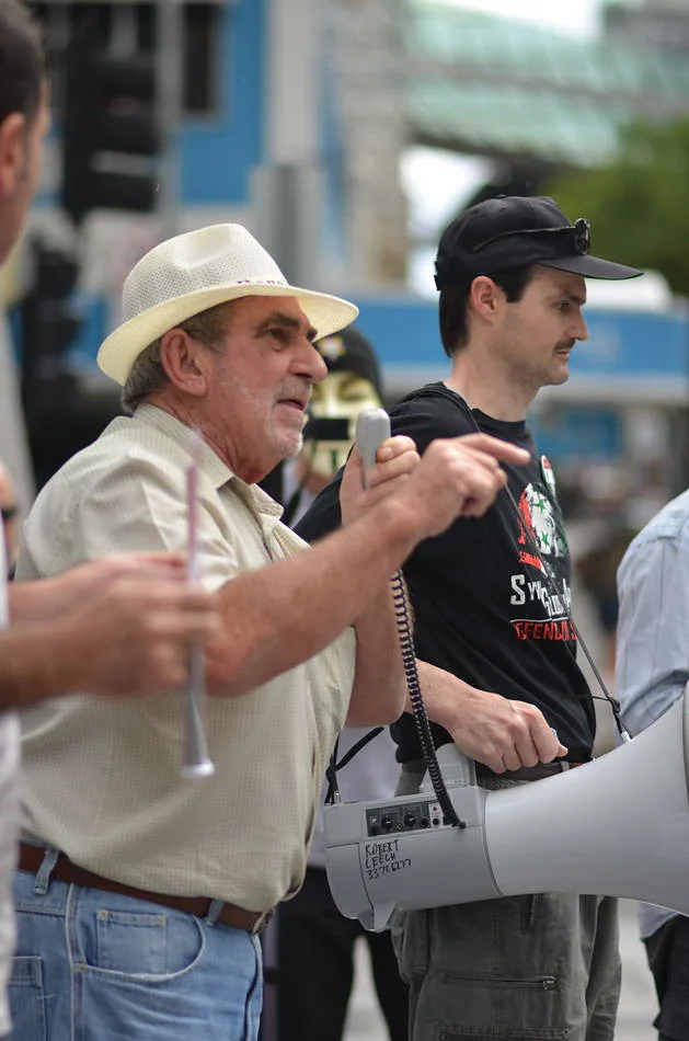 The man in the white hat was speaking into the megaphone with the particular economy of someone who has done this many times and knows how to make a crowd listen.