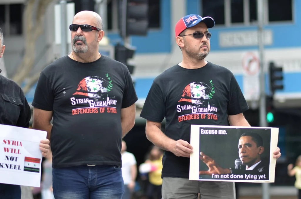Two men in matching 'Syrian Global Army — Defenders of Syria' shirts. They had come a long way in more senses than one to stand in a Brisbane street and say this.
