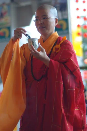 She held the ceremonial bowl with both hands, head slightly bowed. The red robes against the soft background made the frame itself.