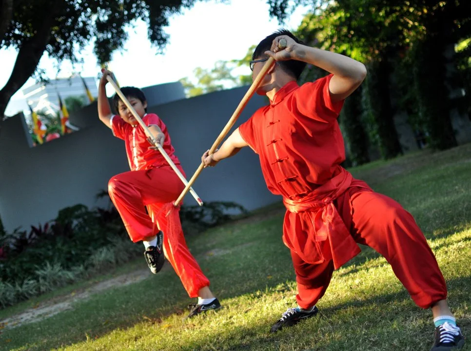 A child and an adult, both in red, crossing bo staffs on a lawn. The kid was completely committed. That commitment is everything.