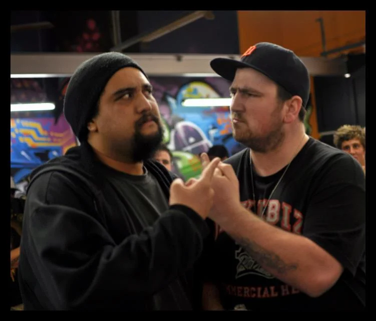 Nose to nose, the graffiti loud behind them. Battle rap face-offs are theatrical but the tension in them is absolutely real.