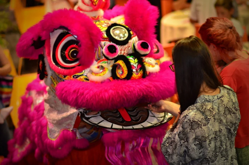 The lion lowered its head to accept an offering from a woman in the crowd. That moment of contact — costume to person — is the whole ceremony.