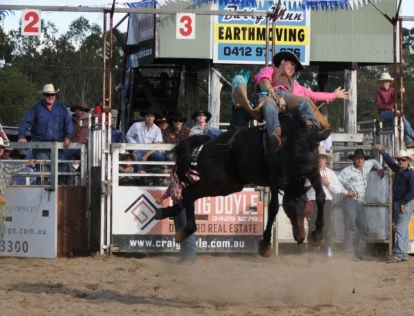 The moment just after the gate opens — horse vertical, rider already working to stay on. The crowd behind the chutes has seen this many times. They still watch.