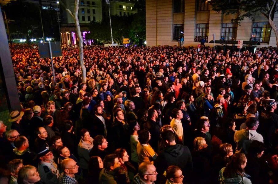 Brisbane at night, seen from a crowd looking the same direction. The city is behind them and they don't care. That's the image.