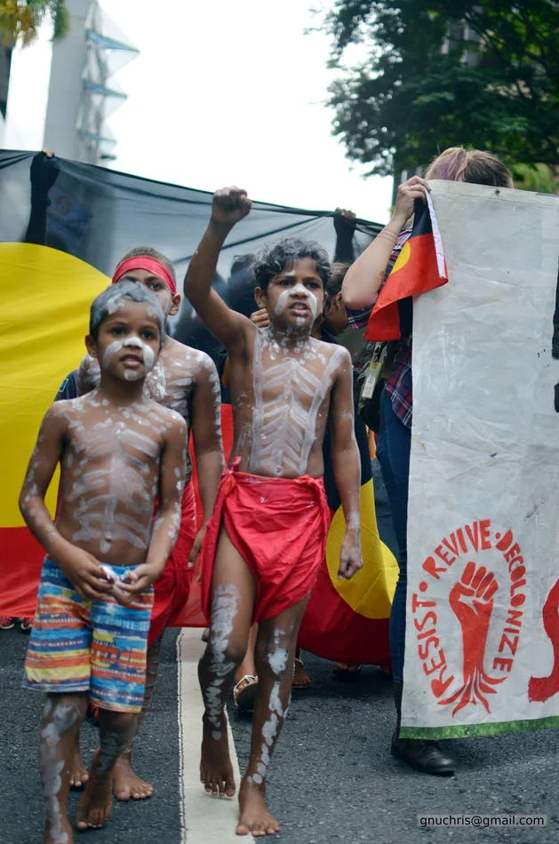 Two children in body paint, one fist raised, the Aboriginal flag stretched out behind them. This is what it means to bring your whole self to a protest.