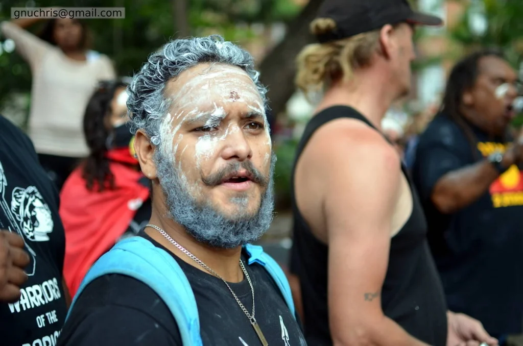 White clay on his face and in his beard, looking directly at the camera. There is nothing ambiguous about where he is or why he is there.