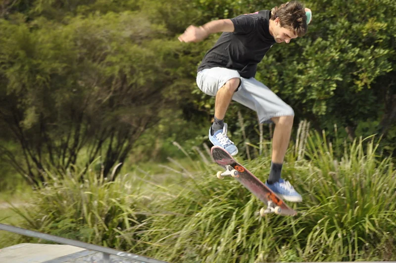 A trick at the park edge, the bush behind him, the board tilted. At a certain point you stop seeing feet and start seeing the shape the body makes.