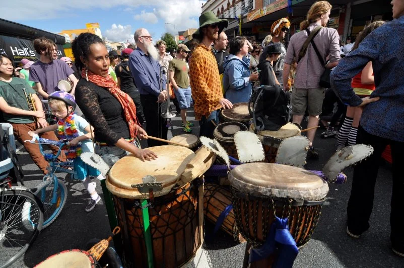 A drummer in the middle of the procession, djembes in a row, the street blocked by sound. The event has its own rhythm.