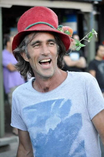 Red hat, plant in the brim, laughing at something off camera. The Kurilpa Derby is the kind of event where this is an unremarkable person to encounter.