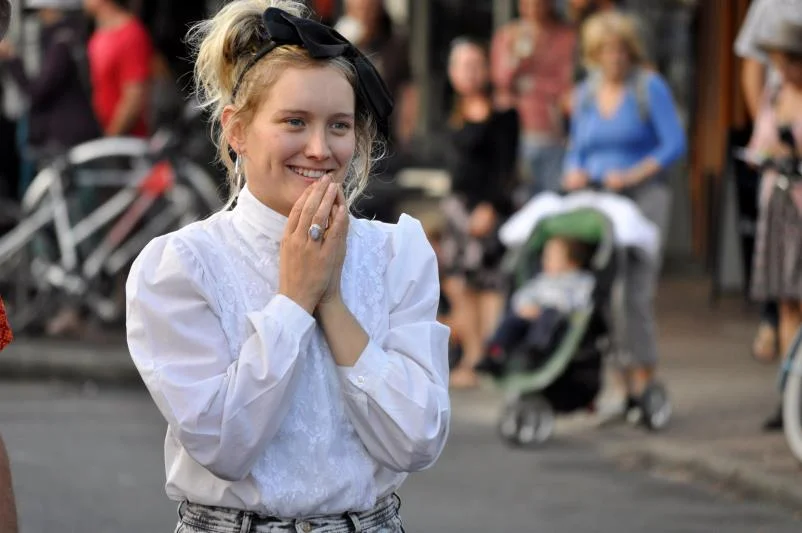 White Victorian blouse, black bow, hands clasped, genuinely delighted by something. This is what West End looks like from the inside.