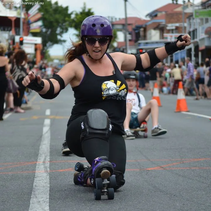 Low and leaning, arms out for balance, purple helmet. Behind her the whole length of Boundary Street is visible. This is her track.