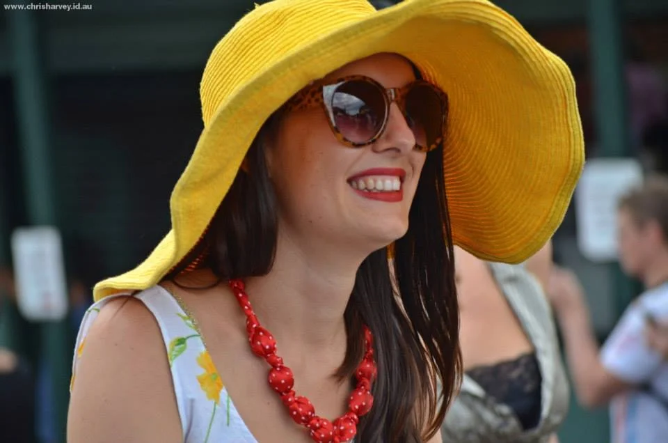 Yellow hat, red necklace, genuine smile at something just off camera. The Kurilpa Derby crowd dresses for the occasion.