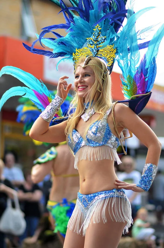 Hands on hips, turquoise feathers, the whole troupe visible behind her. She is completely at home in the middle of a closed street.
