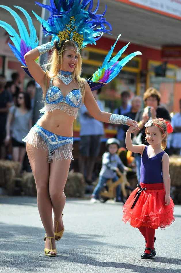 The dancer takes the girl's hand and walks with her down Boundary Street. The girl is in a red tutu and is completely unafraid.