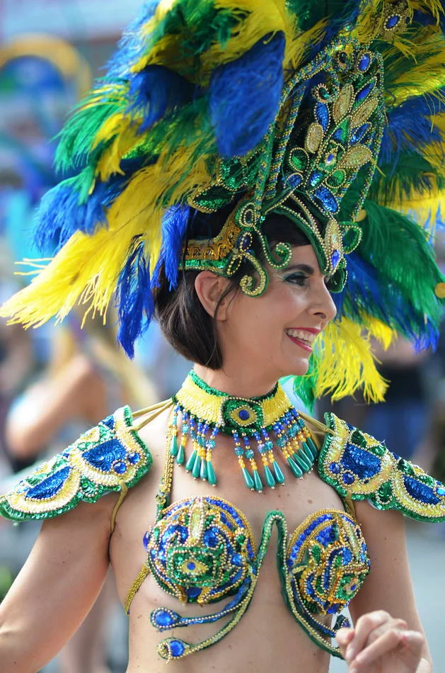 Profile against the blurred crowd. The headdress extends a metre above her head and she carries it as if it weighs nothing.