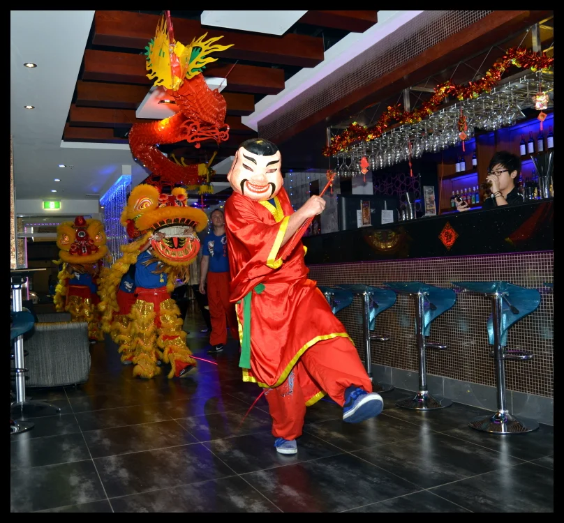 The God of Fortune leads the lion into the restaurant, the bar staff watching from behind the counter. The lion fills the dining room.