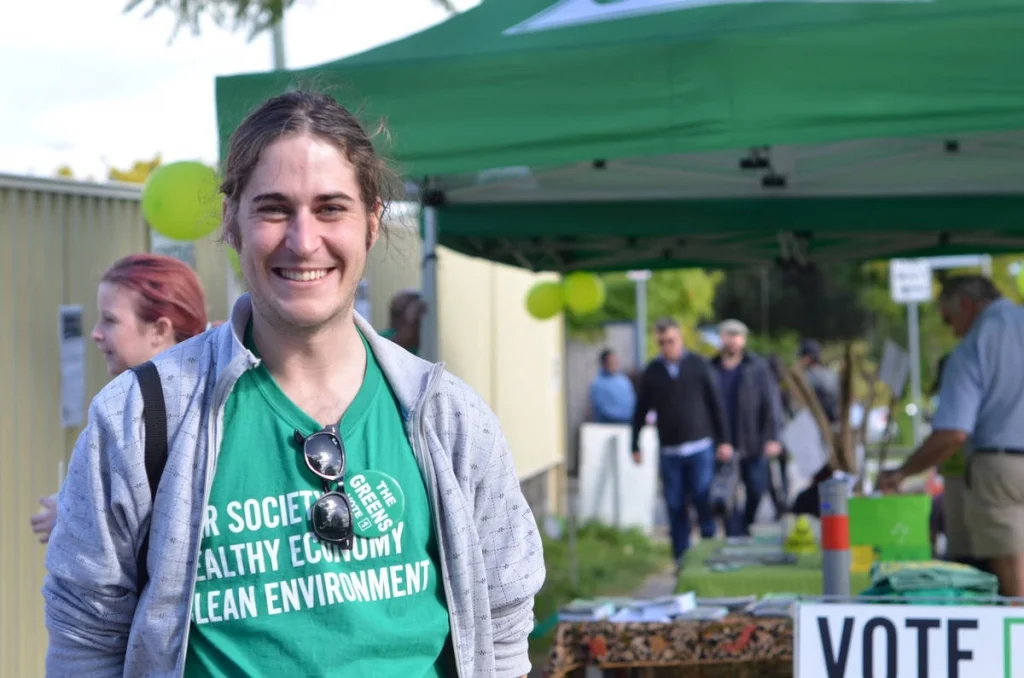 Greens volunteer, genuine smile, the stall behind her. Political presence at a community festival is its own kind of photography.