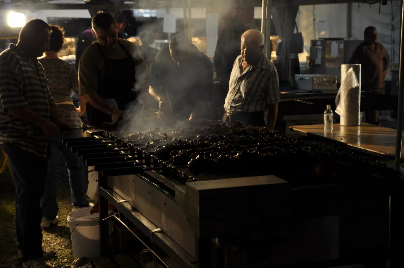 The grill at a Greek festival is not a food stall — it is the centre of gravity. Everyone orbits it sooner or later.