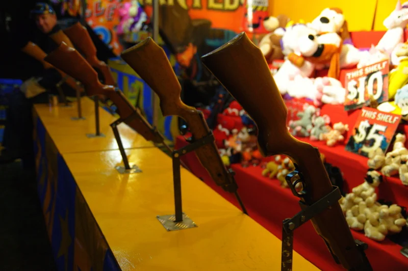 A sideshow alley at midnight has its own peculiar light. The rifles in a row, the stuffed animals, the operator half-awake — there is a photograph in all of it.