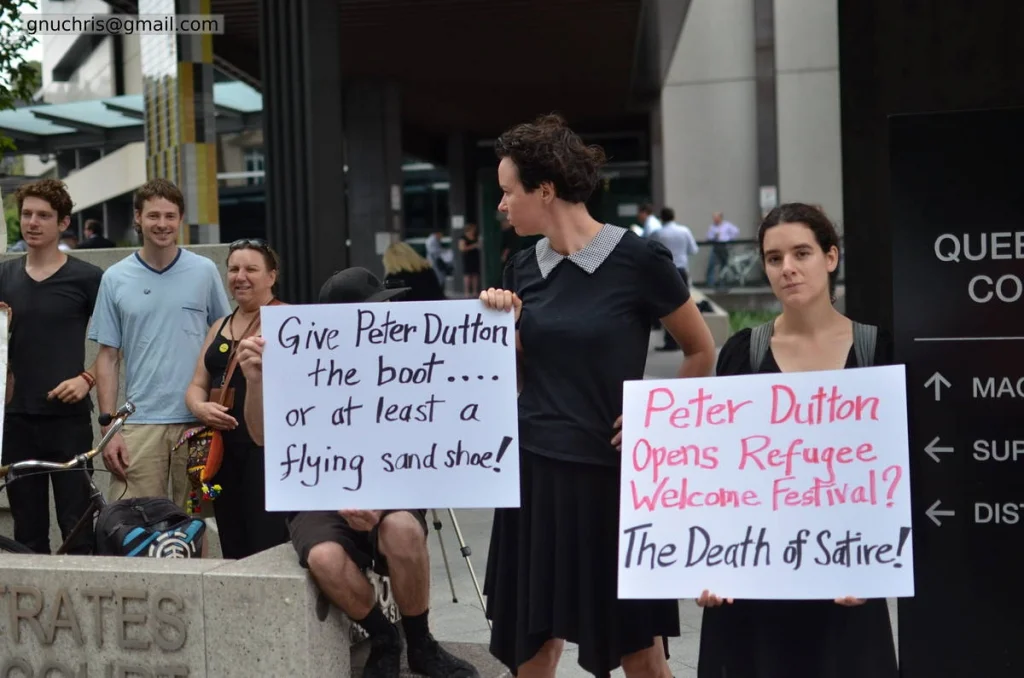 The deadpan sign is a photographic gift. 'Give Peter Dutton the boot — or at least a flying sand shoe' works as an image because the person holding it is completely serious.